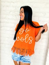 Load image into Gallery viewer, Partial side view of a woman wearing Queen of Sparkles orange fringe sweater vest with 'go vols' text on the front, paired with denim shorts.