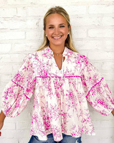 Woman wearing a pink floral blouse against a white brick wall