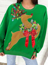 Load image into Gallery viewer, Green sweater with a reindeer design featuring lights and a bow, worn by a person.