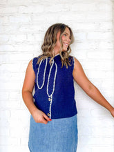 Load image into Gallery viewer, Woman wearing a blue sleeveless top with decorative buttons against a white brick wall.